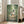 May include: Framed poster displaying animated characters in a lush green bamboo forest scene. Large gray creature with umbrella stands with two children and smaller white creatures on a dirt path. Artwork features rich emerald and forest green tones with Japanese text. Light wood frame leans against white wall next to beige sofa in bright room with tall windows and natural lighting.