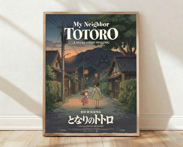 May include: Framed My Neighbor Totoro movie poster featuring two children walking down a twilight village street surrounded by traditional Japanese houses, power lines, and lush green trees. Large glowing eyes peer from the mountainous background. The poster displays both English and Japanese text in white lettering. Warm wooden frame rests against a white wall on light wooden flooring with natural window shadows.
