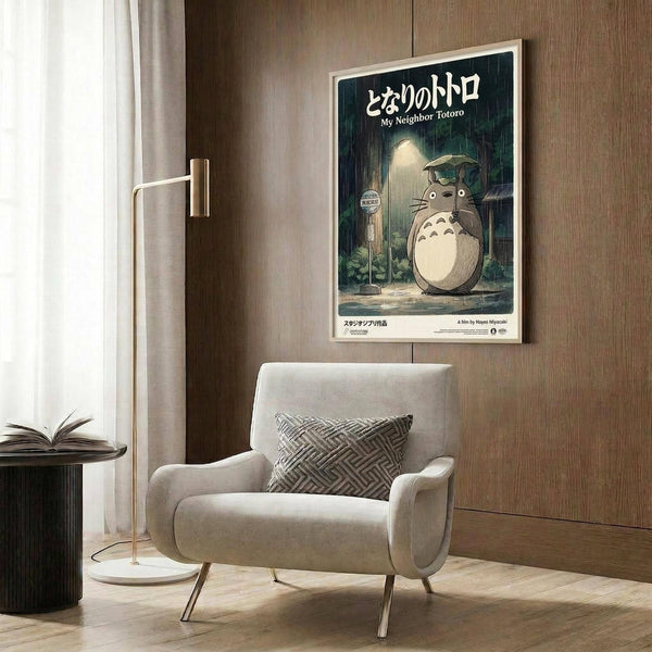May include: Studio Ghibli My Neighbor Totoro movie poster mounted on wood-paneled wall above beige upholstered armchair with geometric patterned pillow. Poster shows iconic Totoro character standing at rainy bus stop with umbrella in dark green tones. Modern living room setting with brass floor lamp, side table with open book, and natural lighting from window with curtains.