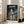 May include: Framed My Neighbor Totoro movie poster leaning against white wall beside beige sofa in bright living room with wooden floors. Poster shows iconic rainy bus stop scene with Totoro, Mei, and Satsuki under red umbrella beneath glowing streetlight, surrounded by dark trees and atmospheric lighting in Studio Ghibli's signature animation style.
