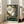May include: Framed My Neighbor Totoro poster leaning against white wall next to beige armchair in bright room with windows. Shows large gray Totoro character sitting in forest tree surrounded by small white spirits, with Japanese text and earthy green and brown tones throughout the vintage-style artwork.