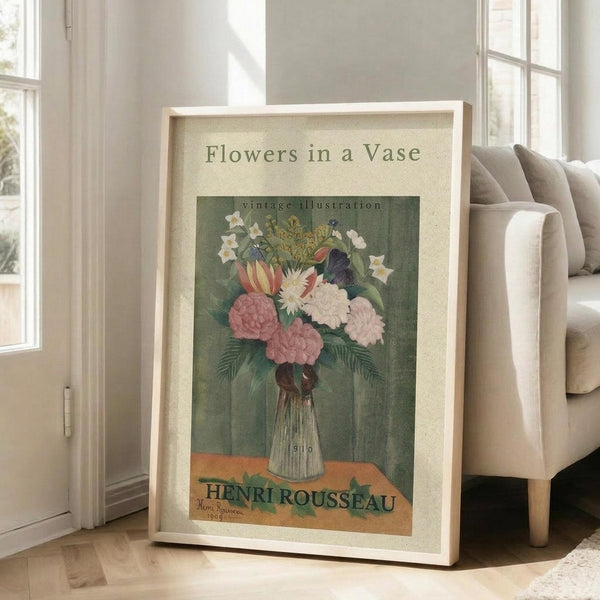 May include: Framed vintage botanical poster featuring colorful flowers in a ribbed glass vase against green background, displayed on light wooden floors next to beige upholstered chair in bright sunlit room with white walls and large windows.