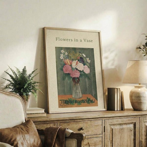 May include: Framed vintage-style botanical print showing colorful flowers in a glass vase, displayed on rustic wood sideboard alongside fern plant, books, and ceramic pottery in neutral-toned living room setting with upholstered furniture