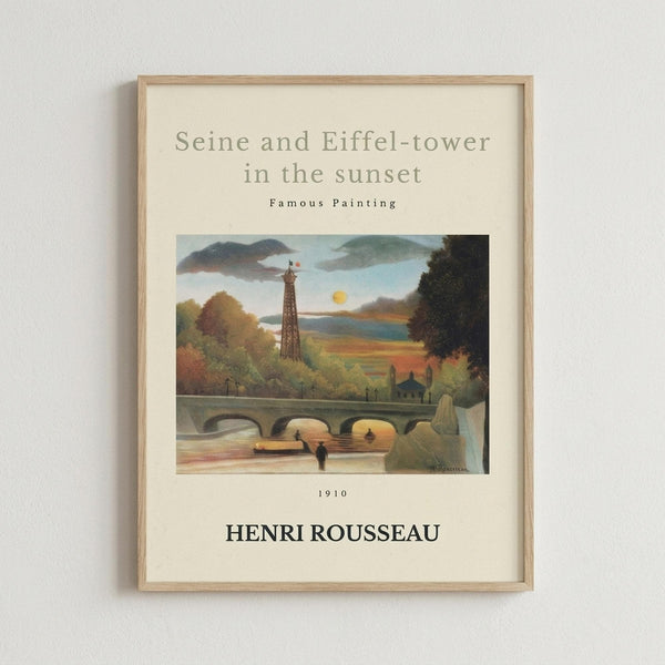 May include: Framed art print mounted on white wall featuring Henri Rousseau's 1910 painting of the Eiffel Tower and Seine River at sunset. The artwork shows a pastoral landscape with the tower rising behind autumn trees, a stone bridge over water, and warm golden sky. Light wood frame with cream matting displays the reproduction with title text above and artist name below the image.