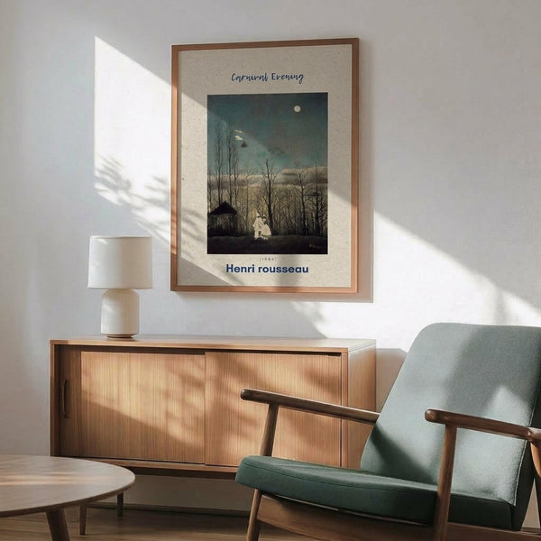 May include: Framed Henri Rousseau poster print featuring a moonlit evening scene with bare trees, small building, and ghostly white figure against dark teal sky. Print has beige matting in thin wooden frame, displayed on white wall above modern wooden credenza with white ceramic lamp. Mint green mid-century armchair with wooden arms sits alongside, bathed in natural sunlight casting geometric shadows across the minimalist room setting.