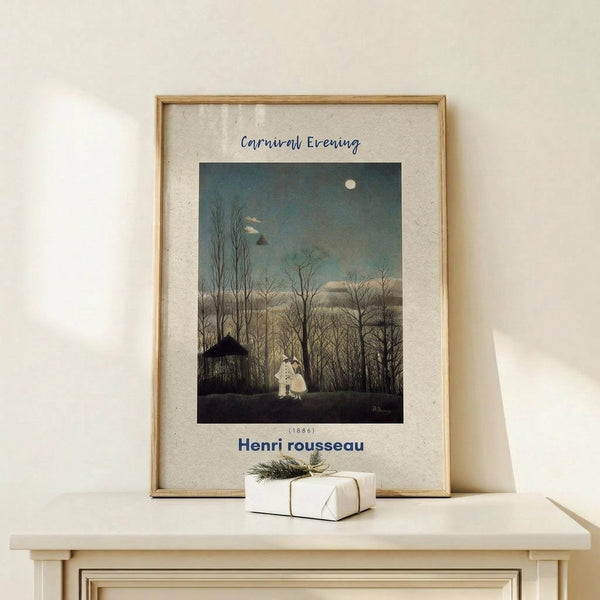 May include: Framed poster print featuring Henri Rousseau's Carnival Evening painting from 1886, showing two figures in white costumes standing among bare winter trees under a moonlit evening sky. The artwork has muted blues, grays, and earth tones. Displayed in a thin wooden frame on a light wood shelf alongside a small white wrapped gift with twine and greenery sprig against a cream wall.