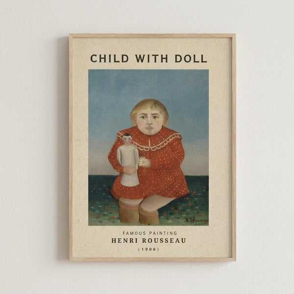 A framed art print showing Henri Rousseau's 1906 painting of a blonde child in a red polka-dotted dress with white lace collar, holding a small doll. The child sits against a blue sky background with green patterned ground. The print has cream matting with "CHILD WITH DOLL" at the top and "FAMOUS PAINTING HENRI ROUSSEAU (1906)" at the bottom, displayed in a light wood frame on a white wall.