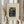 May include: Hands holding a framed vintage art print featuring two figures in a lush jungle setting - a woman in flowing blue robes gesturing upward and a man in dark formal wear. The print has cream matting with "HENRI ROUSSEAU (1909)" at top and "The Muse Inspiring the Poet" at bottom. Natural wooden frame, dried pampas grass visible to the left, soft neutral background with white curtains.