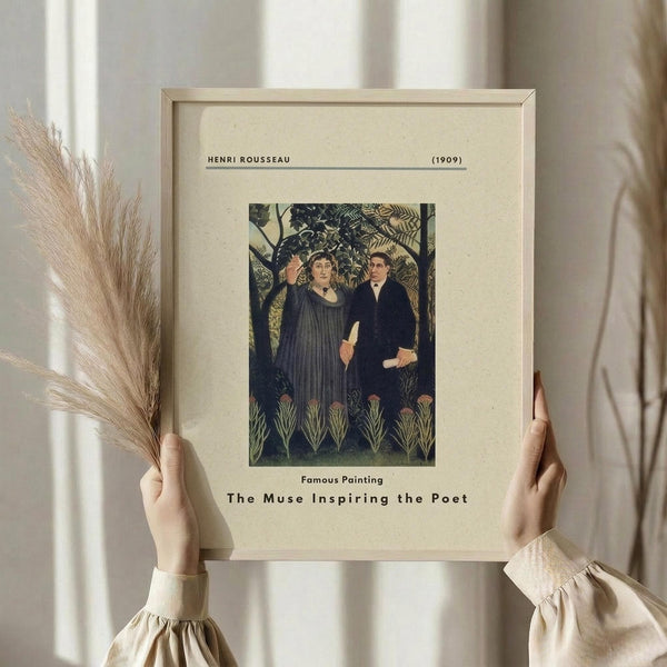 May include: Hands holding a framed vintage art print featuring two figures in a lush jungle setting - a woman in flowing blue robes gesturing upward and a man in dark formal wear. The print has cream matting with "HENRI ROUSSEAU (1909)" at top and "The Muse Inspiring the Poet" at bottom. Natural wooden frame, dried pampas grass visible to the left, soft neutral background with white curtains.