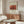 May include: Framed art print featuring Henri Rousseau's "La Guerre" with reddish-orange battle scene artwork and cream background, displayed above a walnut wood credenza in a minimalist living room with white curved chair, glass coffee table, and modern mushroom lamp