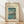 May include: Framed vintage Japanese woodblock print showing Mount Fuji across a lake with cherry blossom tree in foreground, two small boats on blue water, displayed in light wood frame against white textured wall on wooden floor with soft natural lighting creating diagonal shadows