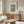 May include: A framed vintage-style Japanese woodblock print poster showing Mount Fuji with a tree and lake in blue and green tones, displayed above a mid-century walnut credenza with sliding doors. The room features a white textured accent chair, glass-top oval coffee table, modern table lamp, and minimalist decor in neutral beige and wood tones.