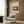 May include: Framed vintage Japanese woodblock print showing moonlit landscape with trees and buildings in earth tones, displayed on wood paneled wall above beige upholstered armchair with geometric patterned pillow, brass floor lamp and side table with open book nearby