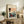 May include: Framed vintage Japanese woodblock print showing a rickshaw scene with figures in traditional dress, displayed on rustic wooden sideboard alongside fern plant, ceramic vase, and books in warm neutral living room setting with beige upholstered chair