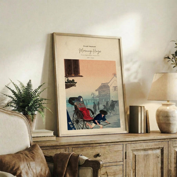May include: Framed vintage Japanese woodblock print showing a rickshaw scene with figures in traditional dress, displayed on rustic wooden sideboard alongside fern plant, ceramic vase, and books in warm neutral living room setting with beige upholstered chair