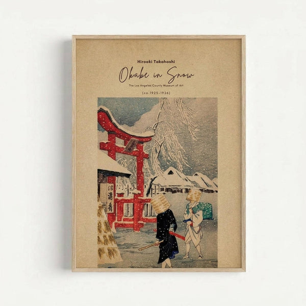 Framed vintage Japanese woodblock print showing a snowy winter scene with a red torii gate, traditional buildings with snow-covered roofs, and two figures in dark clothing walking through falling snow. The artwork features muted colors of red, blue, brown and white against a tan background, displayed in a light wooden frame on a white wall.