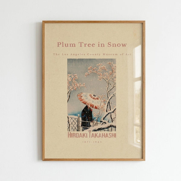 May include: Framed museum poster print mounted on white wall showing Japanese woodblock artwork of figure with red and white umbrella walking past blooming plum tree branches in falling snow. Warm wood frame surrounds cream-colored poster with vintage exhibition styling and artist name at bottom.