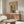 May include: Japanese woodblock print poster featuring snowy shrine scene with red torii gate, figures in winter landscape, and mountain backdrop, displayed in light wood frame above mid-century modern walnut credenza. White mushroom table lamp and brass floor lamp accent the minimal living room with cream chair and glass oval coffee table on light wooden floors.