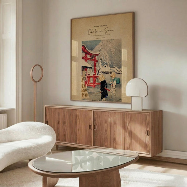 May include: Japanese woodblock print poster featuring snowy shrine scene with red torii gate, figures in winter landscape, and mountain backdrop, displayed in light wood frame above mid-century modern walnut credenza. White mushroom table lamp and brass floor lamp accent the minimal living room with cream chair and glass oval coffee table on light wooden floors.