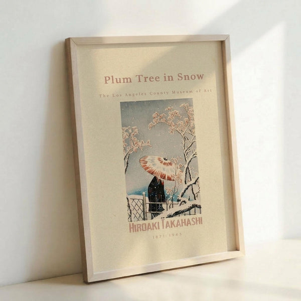 May include: Framed vintage Japanese woodblock print poster featuring a figure with parasol in snowy winter scene with flowering plum tree branches. Natural wood frame against white wall corner, showing muted colors of gray, pink, and blue with delicate snowfall details and traditional artistic style.