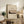 May include: Framed vintage-style art print featuring Mount Fuji with silhouetted trees in muted earth tones, displayed on rustic wooden sideboard alongside fern plant, stacked books, and ceramic vase in neutral-toned living room setting with beige chair and pillow visible