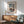 May include: Japanese woodblock print poster showing a traditional temple gate with ornate architecture and snow-covered trees, displayed in wooden frame on white wall above mid-century modern sideboard with ceramic lamp, next to sage green upholstered armchair with wooden frame in sunny room with natural lighting and shadows