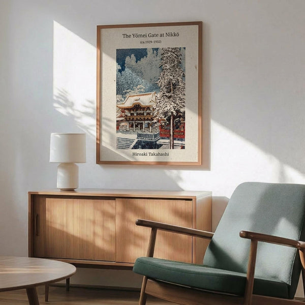 May include: Japanese woodblock print poster showing a traditional temple gate with ornate architecture and snow-covered trees, displayed in wooden frame on white wall above mid-century modern sideboard with ceramic lamp, next to sage green upholstered armchair with wooden frame in sunny room with natural lighting and shadows