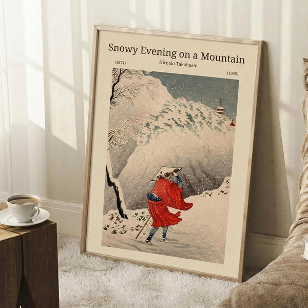 May include: Japanese woodblock print poster in light wood frame leaning against white wall corner, showing figures in red winter clothing walking through snowy mountain landscape with bare trees and falling snow. Small wooden side table with white coffee cup nearby on textured cream rug, cozy beige blanket visible at edge.