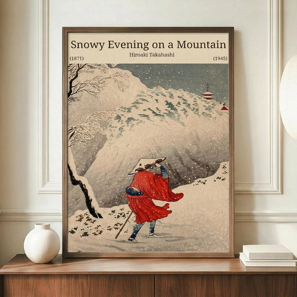 May include: Framed Japanese woodblock print showing figure in red robes walking with staff through heavy snowfall on mountain path, with traditional pagoda visible in distance. Warm beige matting in brown wooden frame, displayed on wooden sideboard next to white ceramic vase and stacked books against cream wall with white trim molding.