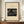 May include: Framed vintage Japanese woodblock print showing a wooden bridge in rain with colorful umbrellas and a large black hat, displayed on wooden sideboard beside white ceramic vase and stacked books against cream paneled wall in modern interior setting.