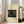 May include: Framed art print leaning against white wall next to beige upholstered chair in bright room with large windows. Print features Japanese woodblock style artwork showing figures with umbrellas on a wooden bridge in rain, with diagonal rain lines across dark sky. Cream colored mat surrounds the artwork in natural wood frame. Sunlight streams across hardwood floors creating geometric shadows.