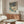 May include: Japanese winter landscape print with snow-covered trees, turquoise stream, and small figures on snowy path, displayed in light wood frame above walnut credenza in modern living room with white curved chair, glass coffee table, and floor lamp