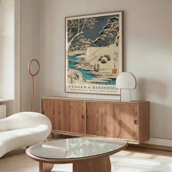 May include: Japanese winter landscape print with snow-covered trees, turquoise stream, and small figures on snowy path, displayed in light wood frame above walnut credenza in modern living room with white curved chair, glass coffee table, and floor lamp