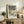 May include: Framed Japanese woodblock print featuring winter landscape with snow-covered trees, blue water, stone lantern, and figures in traditional dress, displayed on rustic wooden sideboard alongside fern plant, ceramic vase, table lamp, and books in warm-toned living room setting