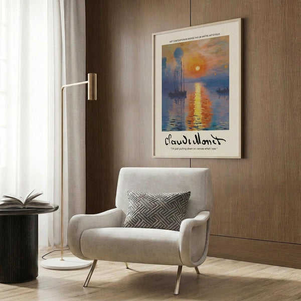May include: Framed Claude Monet poster print hanging on wood-paneled wall above beige upholstered armchair. Artwork shows impressionist sunrise scene with orange sun reflecting on blue water, boats silhouetted against colorful sky. Modern living room setting with brass floor lamp, geometric throw pillow, and dark side table with open book.