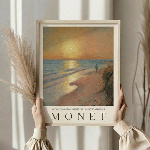 May include: Woman in cream sweater holding framed poster featuring impressionist-style beach sunset scene with golden sky, blue ocean, sandy shore, and solitary figure. Text reads "ART CONTEMPORAIN INSPIRE PAR UN MAITRE ARTISTIQUE MONET" below artwork. Natural wood frame, dried pampas grass visible, soft neutral interior setting with white curtains.