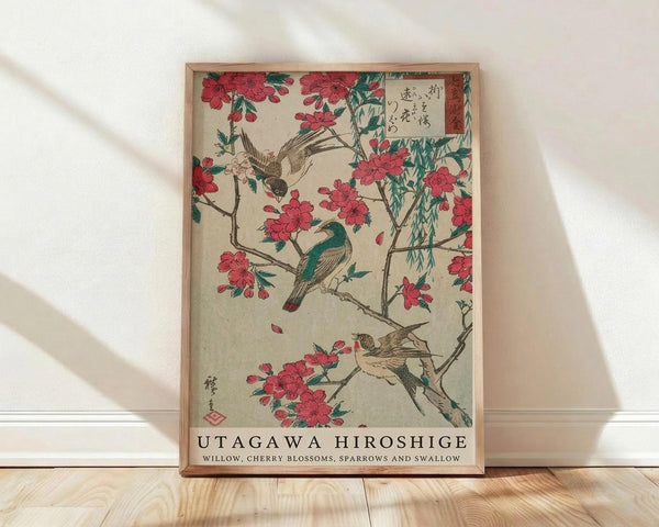 May include: Framed Japanese woodblock print featuring birds perched on flowering cherry blossom branches with willow leaves, displayed against white wall on light wooden floor. Print shows traditional ukiyo-e art style with pink blossoms, green and brown birds, and Japanese text, housed in natural wood frame with museum-style caption below.