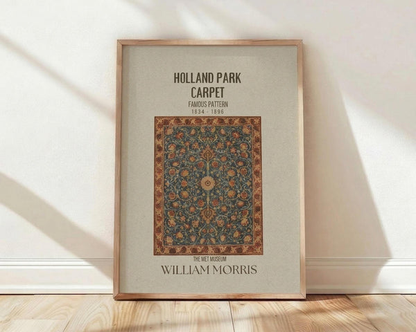 May include: Framed poster featuring an ornate Persian-style carpet design with intricate floral patterns in blues, oranges, and golds on cream background. Text reads "Holland Park Carpet Famous Pattern 1834-1896" and "William Morris The Met Museum." Natural wood frame leans against white wall on light wooden floor with soft window shadows.