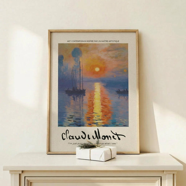 May include: Framed art print featuring an impressionist-style harbor scene at sunrise with sailboats silhouetted against orange and blue waters, displayed on a light wood console table beside a small wrapped gift with twine and pine sprig against a cream wall.