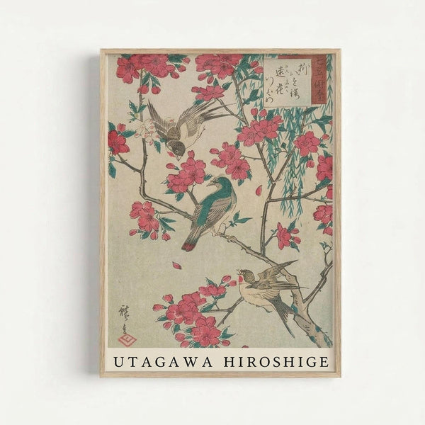 Framed Japanese woodblock print featuring birds perched on flowering cherry blossom branches with drooping willow. Pink cherry blossoms and green leaves against cream background, with Japanese calligraphy in upper right corner. Three birds shown - one teal colored bird on branch and two smaller brown birds, one flying. Traditional ukiyo-e art style in light wood frame with "UTAGAWA HIROSHIGE" text at bottom.
