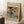 May include: Framed abstract art print with vibrant swirling colors in blues, yellows, reds, and greens, featuring dynamic brushstrokes and geometric shapes. The beige matted poster leans against white wainscoting beside a wooden side table with white coffee cup and saucer, next to a textured beige throw blanket on white carpet.