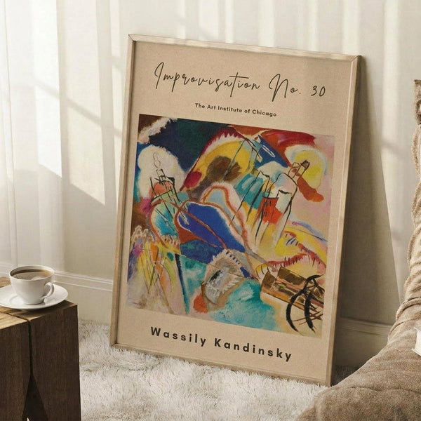 May include: Framed abstract art print with vibrant swirling colors in blues, yellows, reds, and greens, featuring dynamic brushstrokes and geometric shapes. The beige matted poster leans against white wainscoting beside a wooden side table with white coffee cup and saucer, next to a textured beige throw blanket on white carpet.