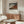 May include: Japanese woodblock print poster of Mount Fuji with red mountain peak and blue cloudy sky, displayed in thin wooden frame above walnut credenza. Modern living room with cream curved chair, glass oval coffee table, and brass floor lamp. Minimalist Scandinavian interior with white walls and natural light from window.