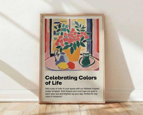 May include: Framed poster print in light wooden frame leaning against white wall on light wood floor. Artwork shows colorful still life with red flowers in orange vase, blue teapot, green pitcher, and fruit on pink tablecloth, painted in Matisse-inspired style with bold colors and simplified shapes. Below artwork is title "Celebrating Colors of Life" with descriptive text about the Matisse-inspired design.