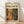 May include: Framed poster leaning against white wall on light wood floor. Poster features abstract expressionist artwork with chaotic paint splatters and drips in orange, black, green, and cream colors. Text reads "POLLOCK" in large black letters with "CHAOS AND CREATIVITY 1912-1956" above. Natural wood frame with cream matting. Soft natural lighting creates gentle shadows on textured white fabric backdrop.