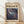 May include: Framed art poster displaying an abstract composition with swirling blue, purple, and navy tones interspersed with white paint splatters and golden yellow dots. The artwork features flowing, cosmic-like patterns reminiscent of galaxies or nebulae. Text reads "CHAOS AND CREATIVITY" and "POLLOCK" with dates "1912-1956" on cream-colored background. Natural wood frame sits against white wall on light wooden floor with soft window light creating diagonal shadows.