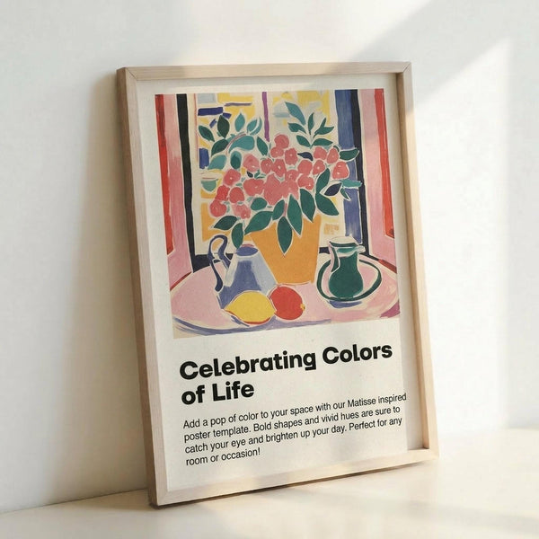 May include: Framed poster print in light wood frame leaning against white wall. Colorful still life artwork shows red flowers in yellow vase, blue and green pitchers, yellow and red fruits on pink tablecloth with vertical stripes in background. Bold, flat colors in Matisse-inspired style. Black text below reads "Celebrating Colors of Life" with descriptive paragraph about adding color to spaces.