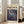 May include: Framed abstract art poster with swirling blue, purple, and gold paint splatters in cosmic pattern, displayed in light wooden frame leaning against white wall next to beige upholstered chair in bright, minimalist living room with hardwood floors and large windows