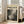 May include: Framed art print with "POLLOCK" text and "CHAOS AND CREATIVITY 1912-1956" subtitle above abstract black and gray paint splatter artwork, displayed in light wood frame leaning against white wall next to beige upholstered chair in bright living room with windows and hardwood floors