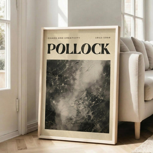 May include: Framed art print with "POLLOCK" text and "CHAOS AND CREATIVITY 1912-1956" subtitle above abstract black and gray paint splatter artwork, displayed in light wood frame leaning against white wall next to beige upholstered chair in bright living room with windows and hardwood floors